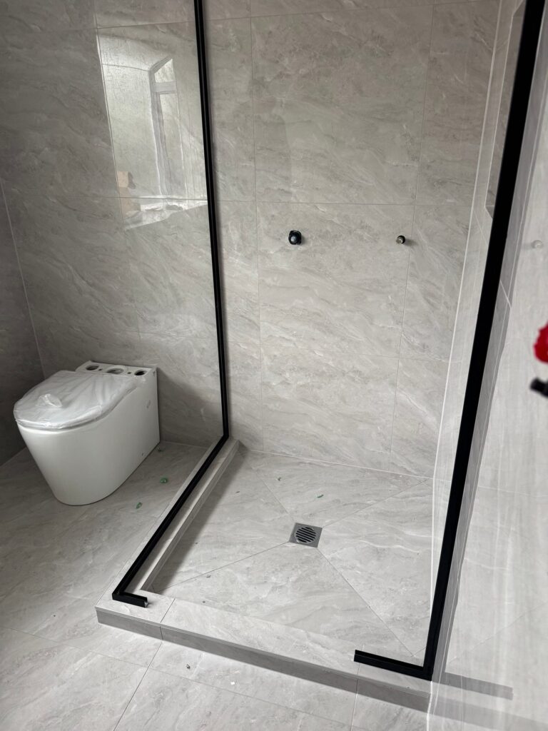 Tiled bathroom with walk-in shower and wall-hung toilet in Pakuranga